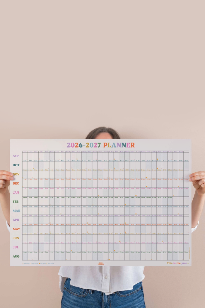 person holing large calendar print against a pink wall