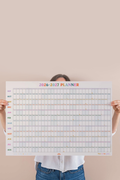 person holing large calendar print against a pink wall