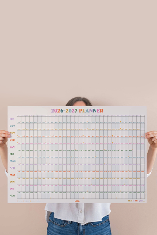 person holing large calendar print against a pink wall