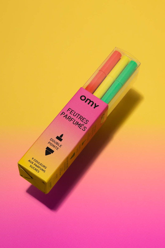 Pack of colorful scented markers with 'omy' branding on a gradient yellow to pink background