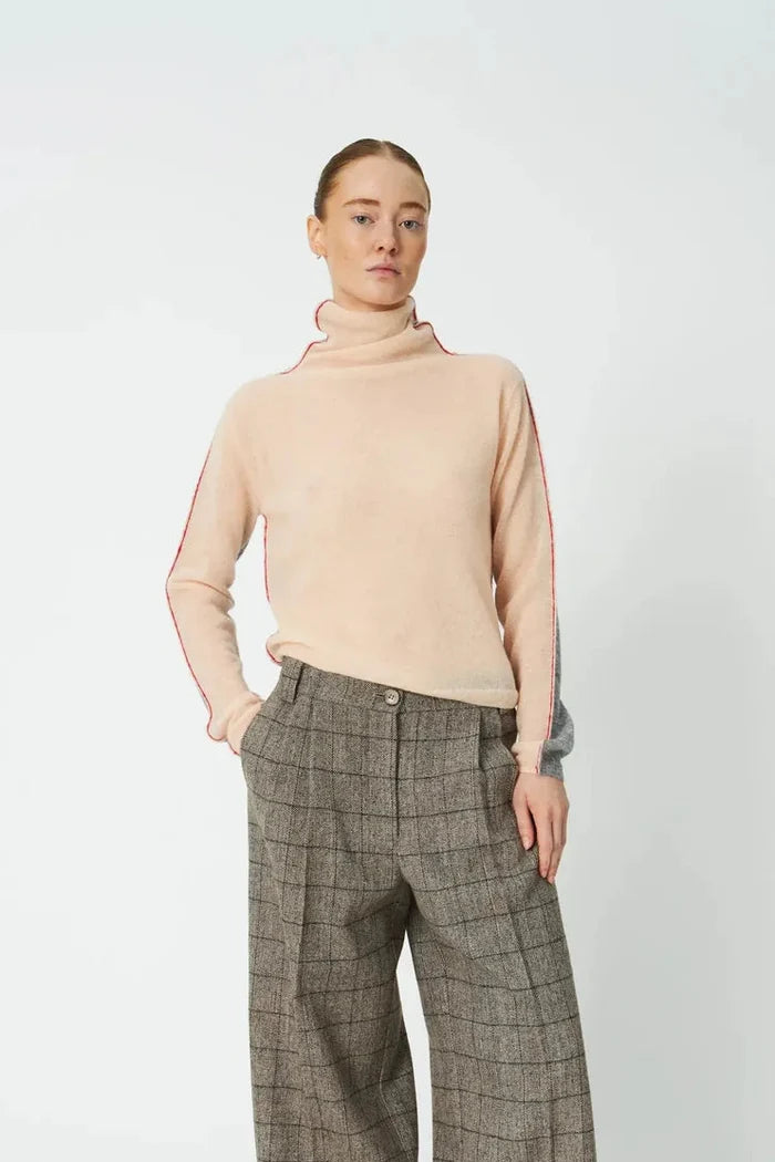 Woman wearing Pale Pink turtleneck and slacks against a white background