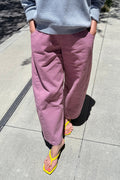 A person outdoors wearing loose, wide-leg dusty pink pants with a light blue ribbed sweatshirt and bright yellow thong sandals on a paved walkway.