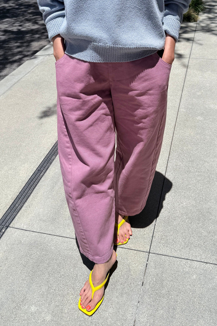 A person outdoors wearing loose, wide-leg dusty pink pants with a light blue ribbed sweatshirt and bright yellow thong sandals on a paved walkway.