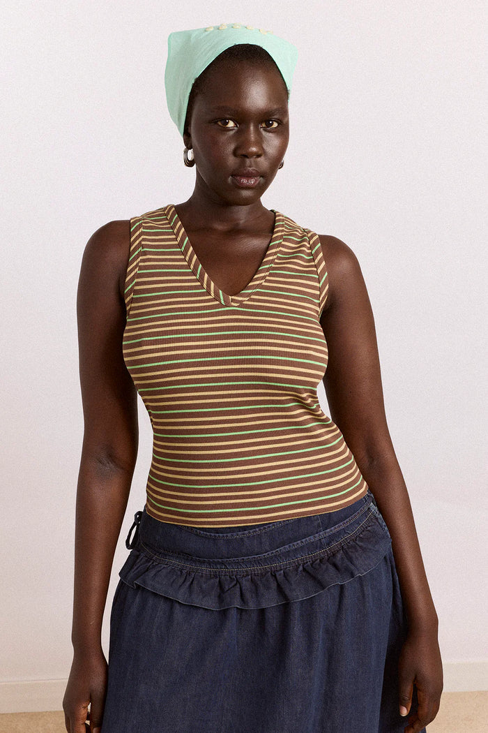 Woman wearing a striped tank top and blue skirt with a light green headscarf against a white background