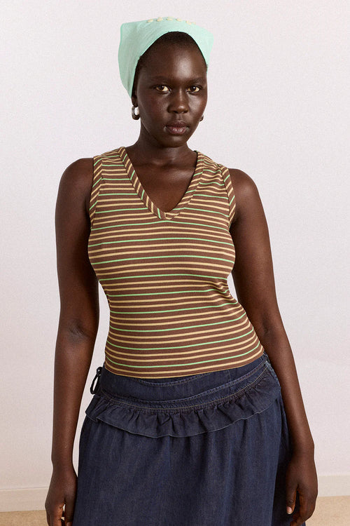 Woman wearing a striped tank top and blue skirt with a light green headscarf against a white background