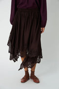 Person wearing a dark purple top and brown lace skirt on a white background