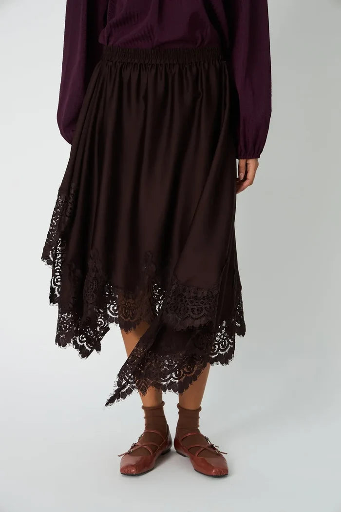 Person wearing a dark purple top and brown lace skirt on a white background