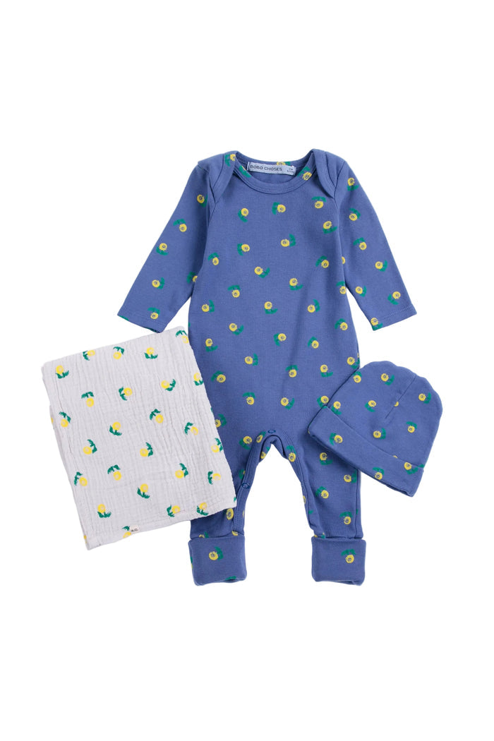 A baby three-piece outfit set featuring a long-sleeve footless romper in dusty blue with a yellow and green flower print, a matching blue bonnet, and a white muslin blanket with a matching flower print, laid out on a white background.