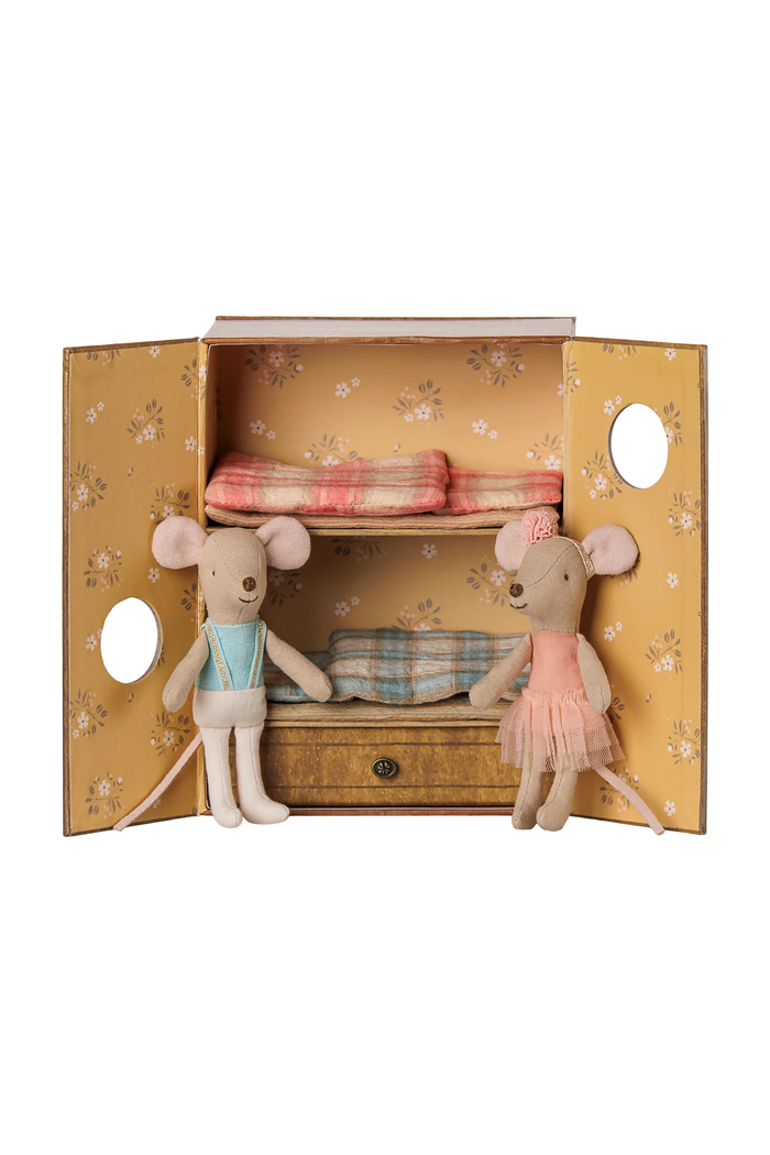 A miniature dollhouse-style cabinet with floral yellow doors, two shelves, and a small drawer, styled with two plush mice and folded bedding in soft pastel colors on a white background.