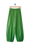Green wide-leg sweatpants with an elastic waistband and elastic ankle cuffs, hanging from a wooden hanger against a plain white wall.