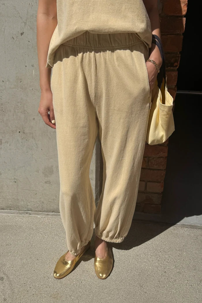 Person wearing pale yellow pants and a matching top, standing against a concrete wall.