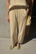 Person wearing pale yellow pants and a matching top, standing against a concrete wall.