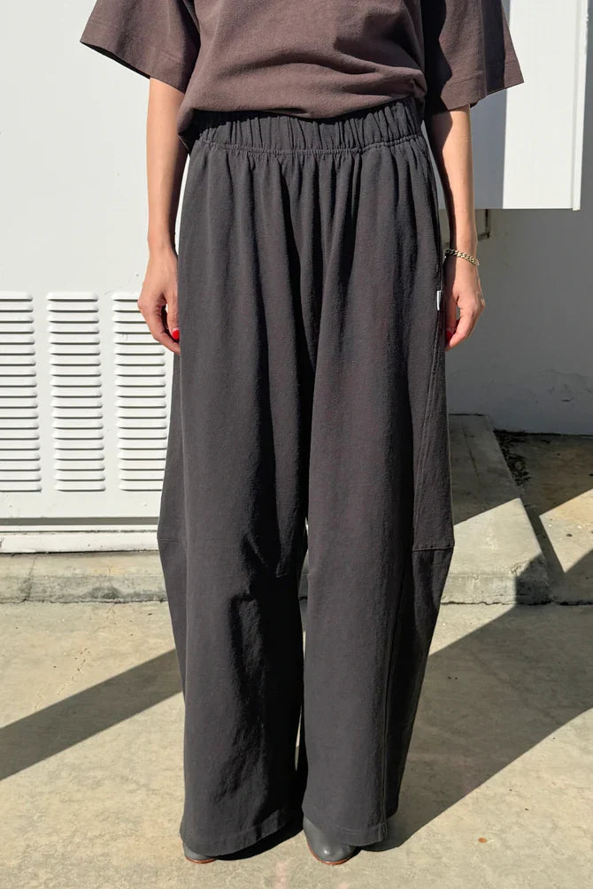 Person wearing a brown top and dark gray wide-leg pants standing outdoors.