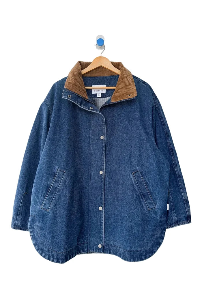 A blue denim jacket with a brown corduroy collar, hanging on a wooden hanger against a light gray background.