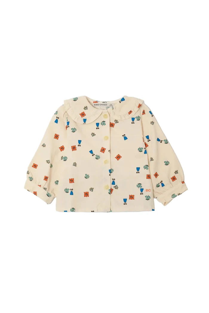 A cream-colored long-sleeve button-up shirt for toddlers, featuring a Peter Pan collar and an all-over colorful print of small characters and shapes, laid flat against a light gray background.