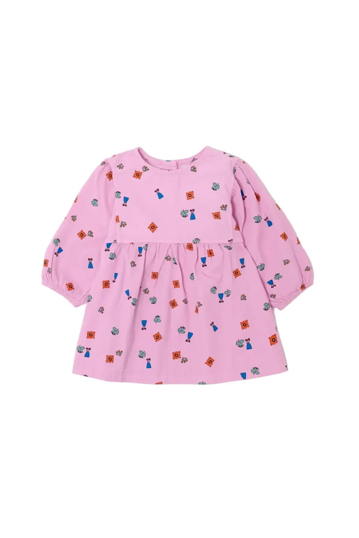 A pink long-sleeve baby dress with an all-over small colorful pattern of tiny figures and shapes, featuring a gathered waist seam and front pockets, shown on a light gray background.