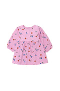 A pink long-sleeve baby dress with an all-over small colorful pattern of tiny figures and shapes, featuring a gathered waist seam and front pockets, shown on a light gray background.