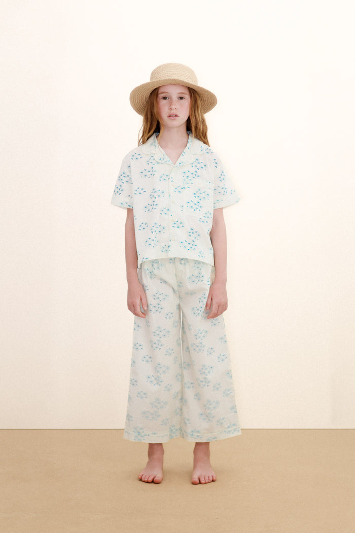 Young girl wearing a floral pajama shirt and wide-leg pajama pants with a hat on a beige background