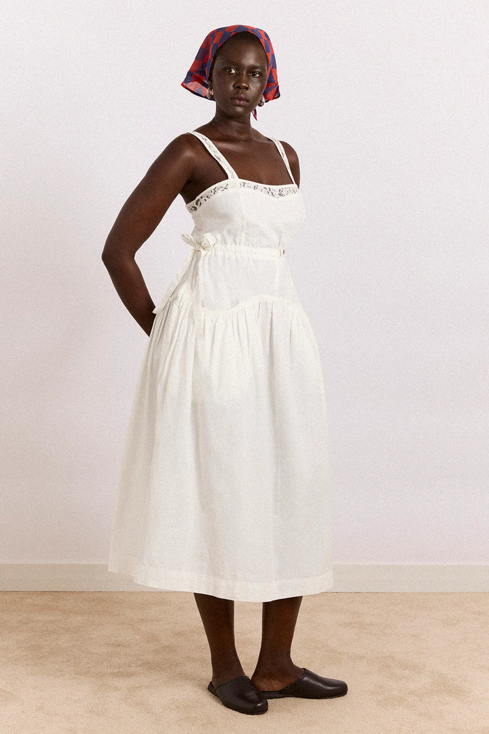 Woman wearing a white dress with a red and blue headscarf against a plain background
