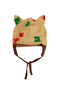 A beige knit baby hat with cat ears and brown chin ties, decorated with small green and red cartoon cat prints, shown on a plain white background.