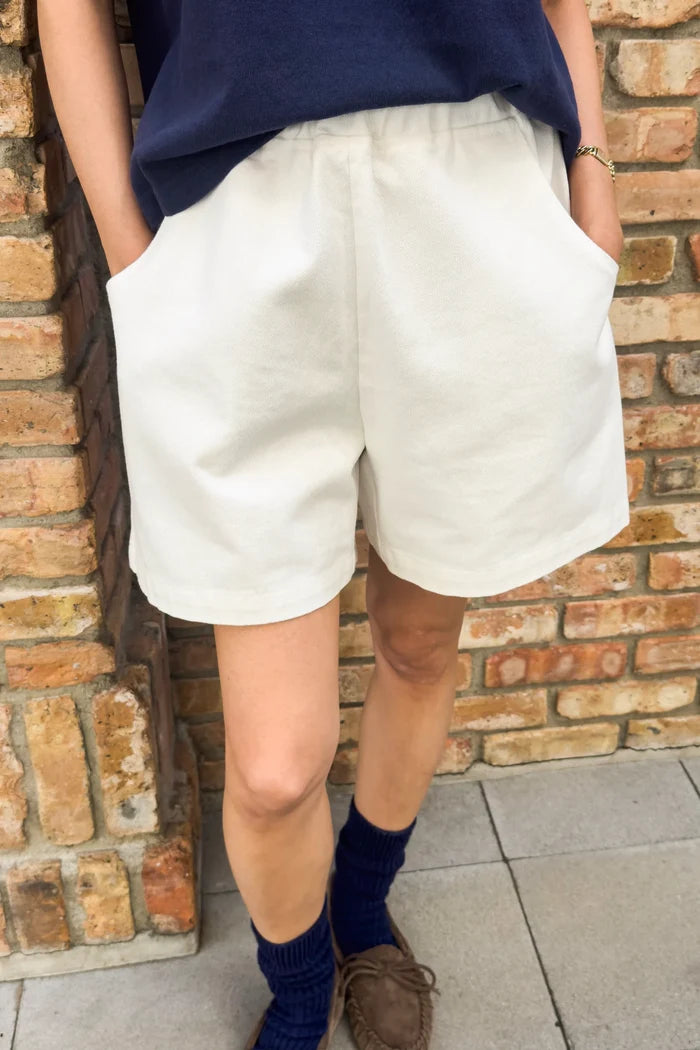 Person wearing white shorts and navy top against a brick wall.