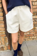 Person wearing white shorts and navy top against a brick wall.