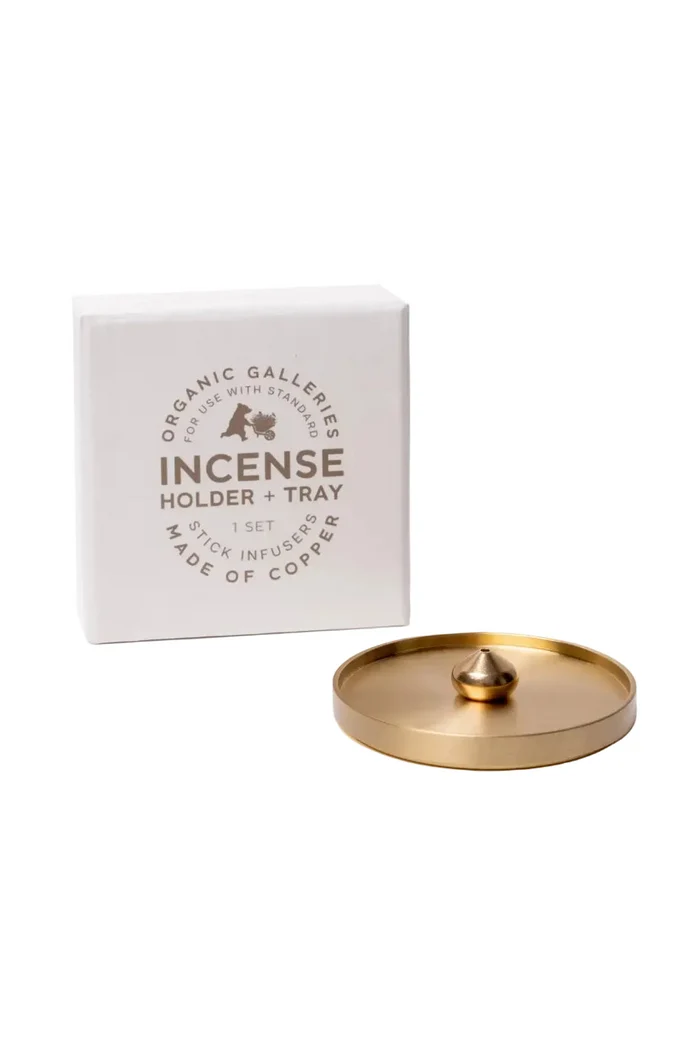 A white square product box labeled 'Organic Galleries Incense Holder + Tray' next to a round brass-colored incense holder tray with a small central knob, on a clean white background.