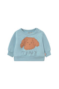 A light blue long-sleeve baby sweatshirt featuring a graphic of a fluffy orange-brown dog head and the word 'TINY' printed below it, displayed on a clean off-white background.