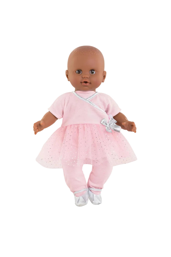 A baby doll with a bald head and dark skin wearing a light pink outfit with a tutu skirt, white bow, and white shoes, photographed against a plain white background.