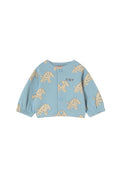 A light blue baby cardigan featuring a repeating beige dog print and the word 'TINY' embroidered on the chest, displayed flat against a warm off-white background.
