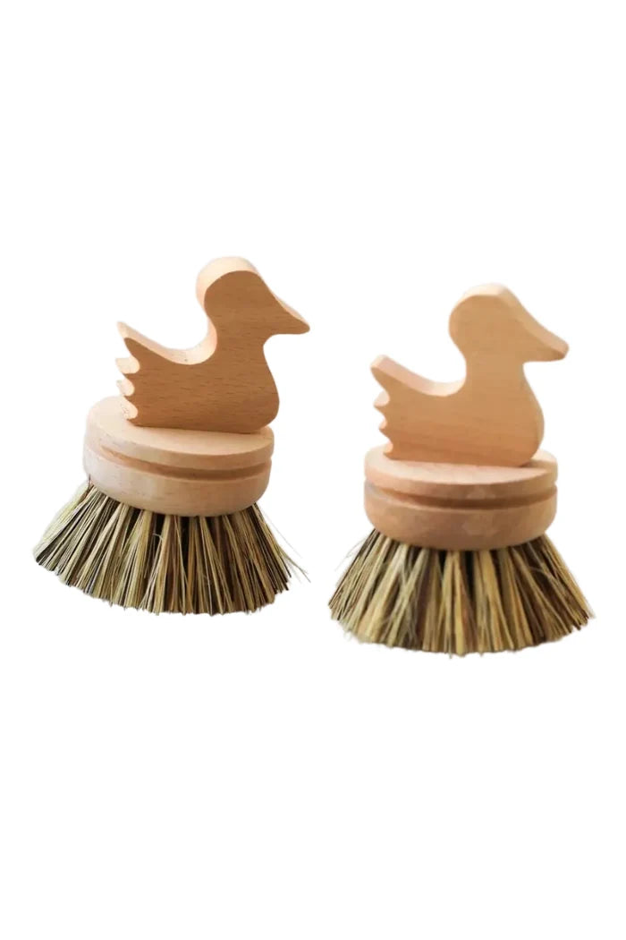 Two wooden dish brushes shaped like ducks on a marble surface.