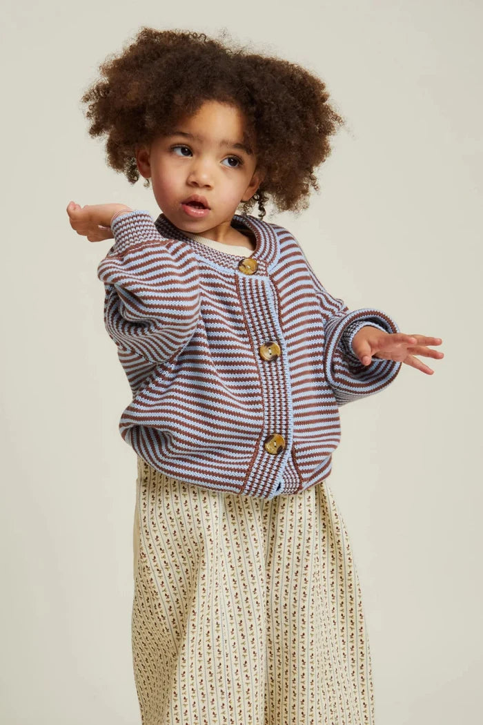 Child wearing a striped sweater and beige pants on a plain background