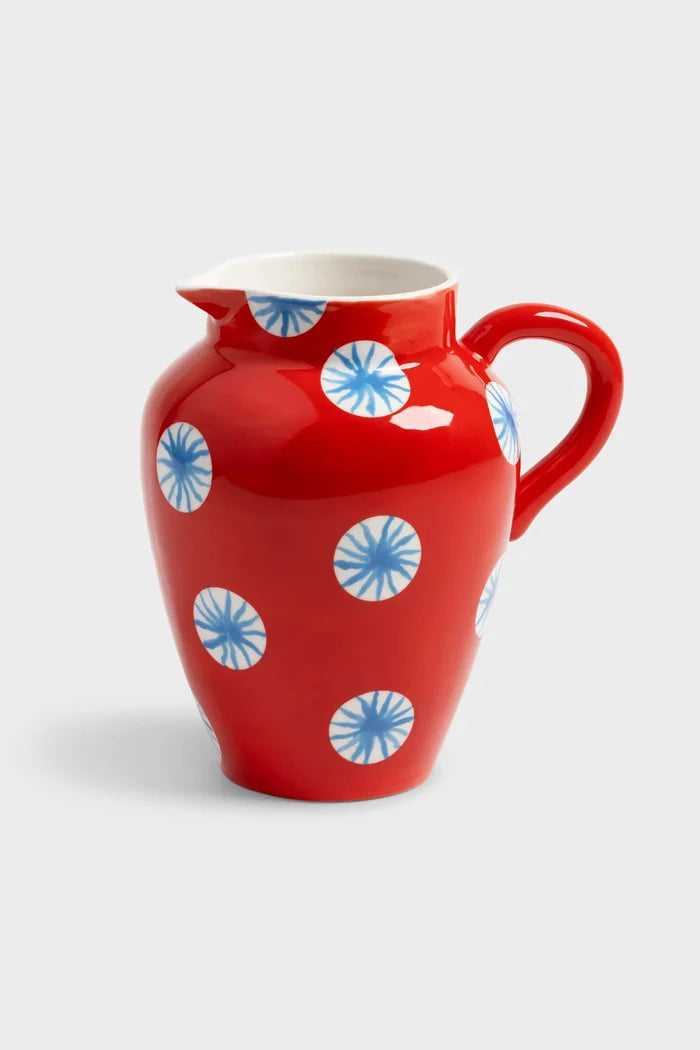 Red ceramic pitcher with blue sun pattern on white background