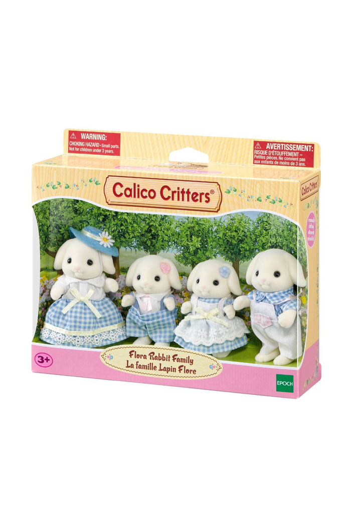 Calico Critters 'Flora Rabbit Family' toy set in its original window box packaging, featuring three rabbit figures in blue and white outfits on a green forest background.