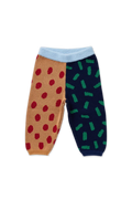 A pair of split-pattern knit pants for babies, featuring one leg in tan with red polka dots and the other in navy with green dash patterns, finished with a light blue ribbed waistband.