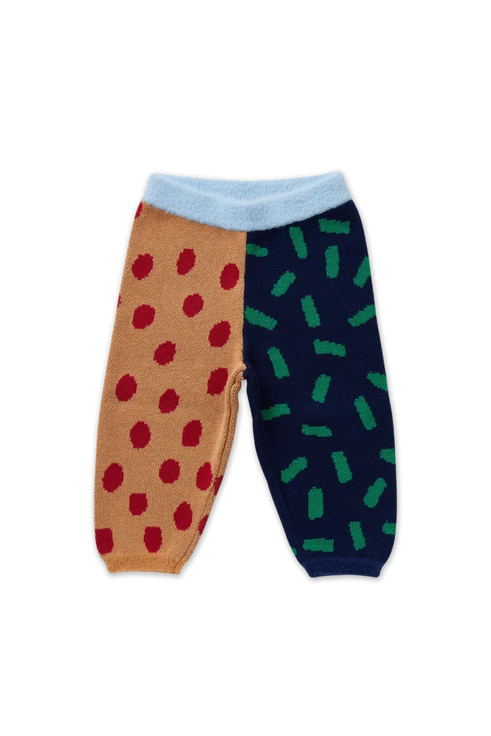 A pair of split-pattern knit pants for babies, featuring one leg in tan with red polka dots and the other in navy with green dash patterns, finished with a light blue ribbed waistband.