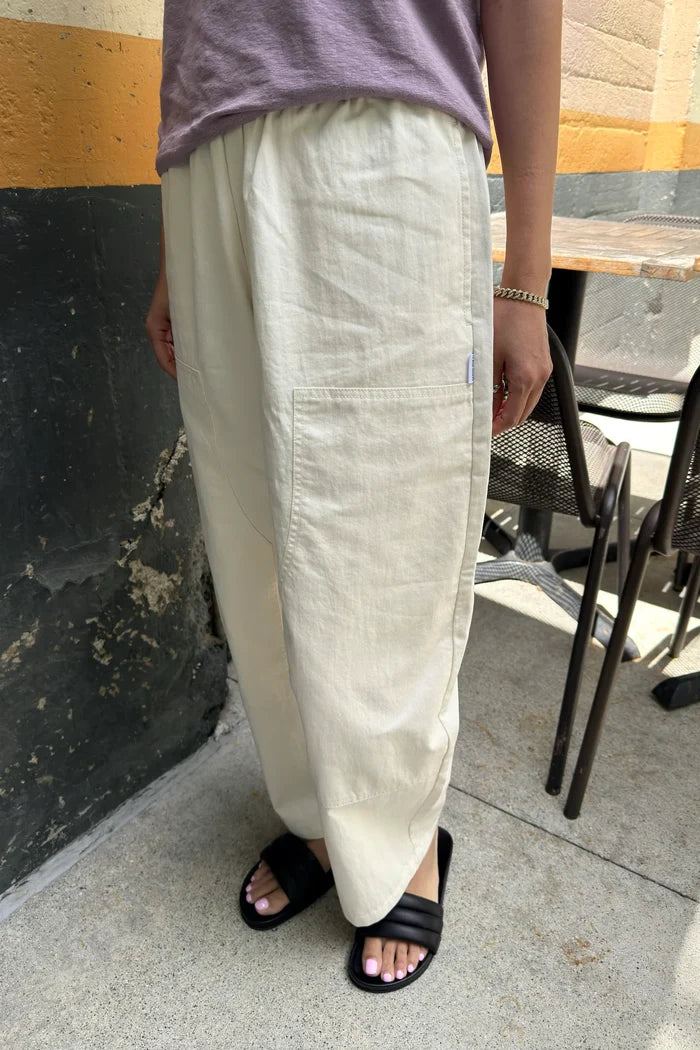 Person wearing white pants and black sandals standing on a sidewalk.