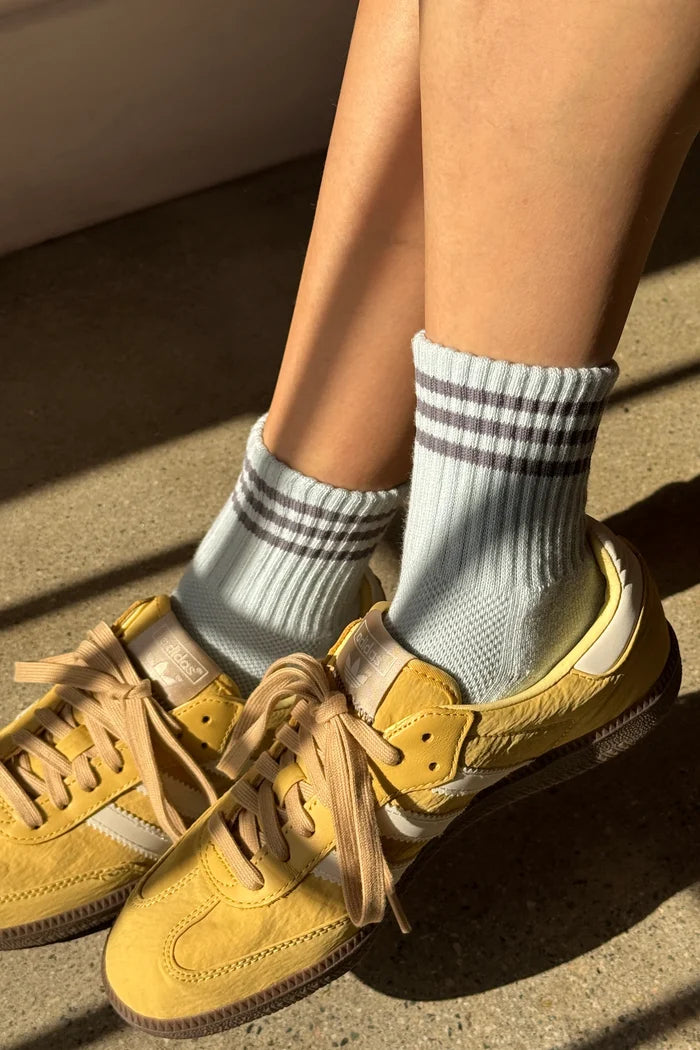 Yellow sneakers worn with light gray socks featuring dark gray stripes on a concrete surface.