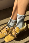Yellow sneakers worn with light gray socks featuring dark gray stripes on a concrete surface.