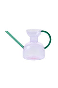 Clear glass watering can with green handle and spout on a white background