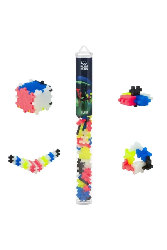 A set of glow-in-the-dark plastic building blocks shown in a clear cylindrical tube with a black label, plus several example assembled structures on a white background. The visible text on the tube reads PLUS PLUS.