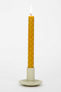 Yellow polka dot candle in a beige holder on a light gray background