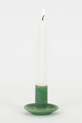 Green ceramic candle holder with a white candle on a white background