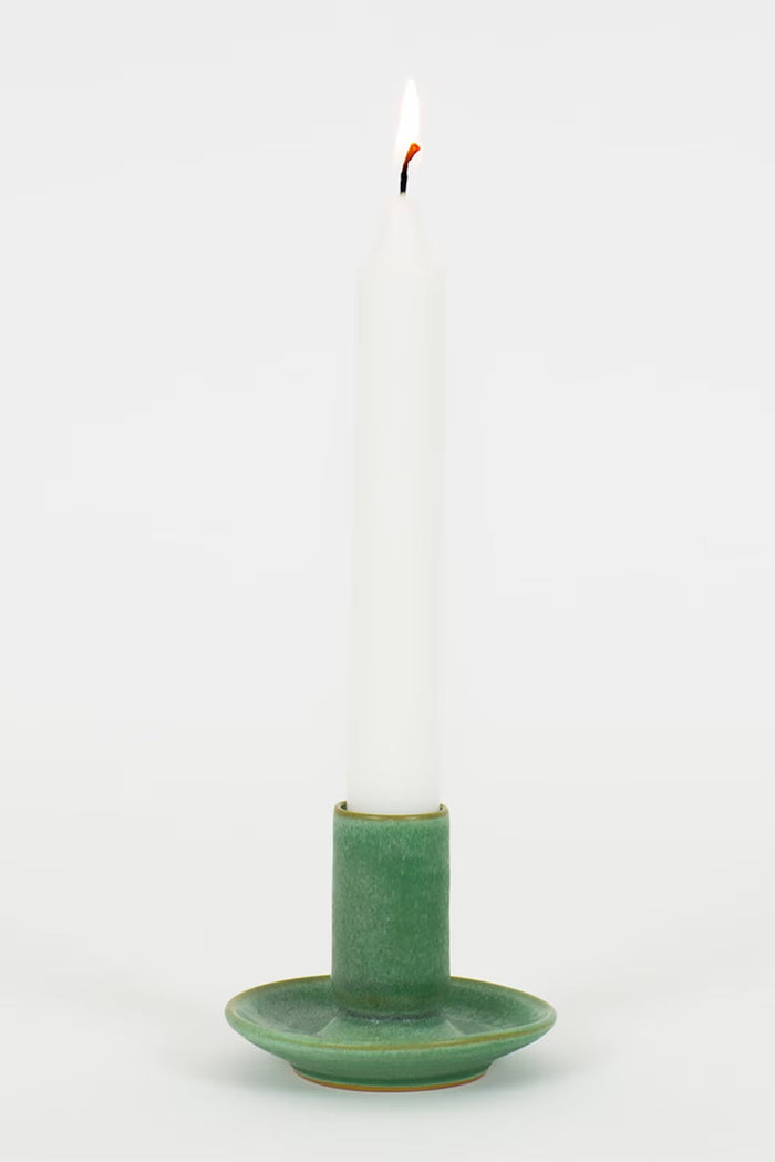 Green ceramic candle holder with a white candle on a white background