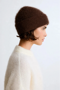 Person wearing a brown knitted beanie and white sweater against a light background