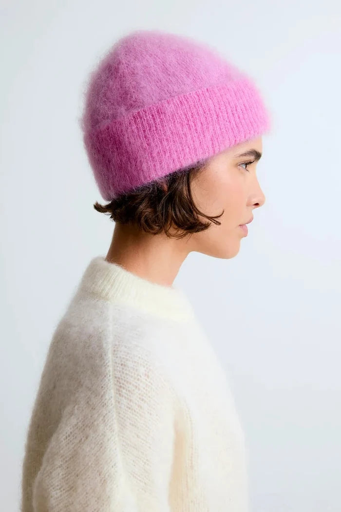 Woman wearing a pink knitted hat and white sweater against a light background