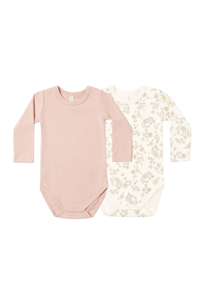 Two long-sleeve baby bodysuits laid flat on a white background. The front bodysuit is a solid dusty pink, and the back bodysuit is off-white with a delicate beige floral pattern.