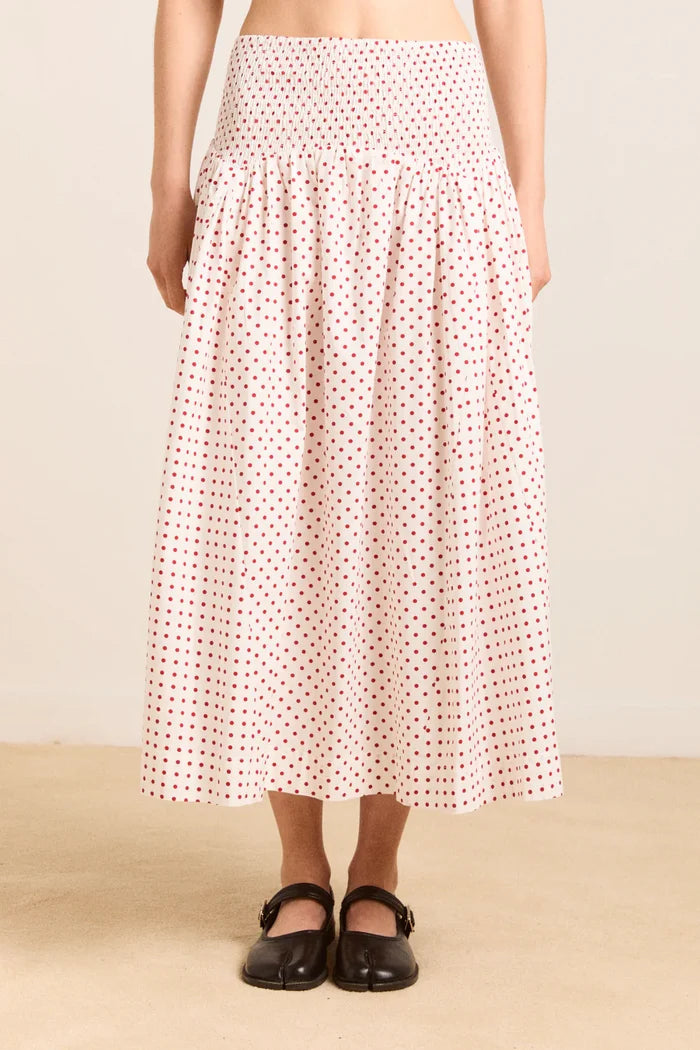 Person wearing a white skirt with red pattern on a beige background