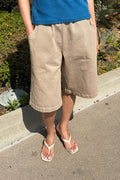 Woman standing on the sidewalk, wearing khaki shorts and heels.