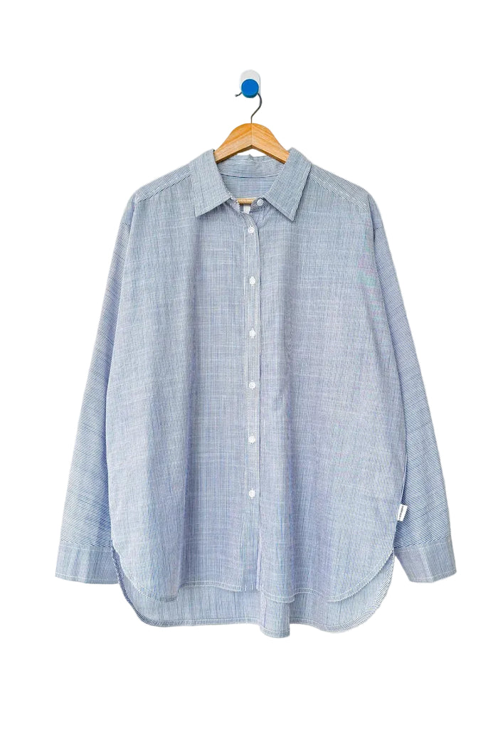 A light blue and white textured button-up shirt hanging on a wooden hanger against a plain white wall.